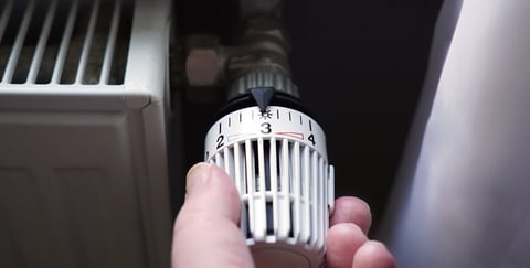 Person dreht an Regler von Heizkörper